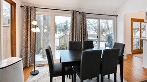 A dining area with a table and chairs, large windows with curtains, and a view of the outside.
