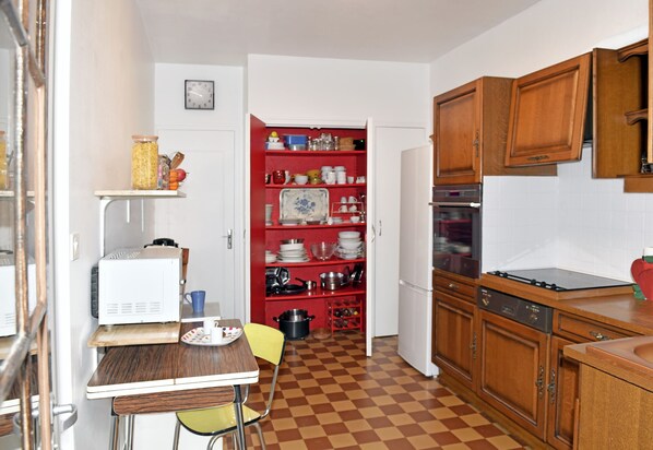 A compact kitchen with wooden cabinets, a microwave, and a red shelf unit.