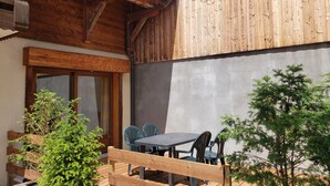 Eine Holzhütte mit einer Terrassenfläche, ausgestattet mit Tisch und Stühlen, umgeben von viel Grün.