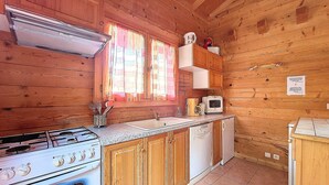 A wooden cabin kitchen with a stove, sink, and white appliances.
