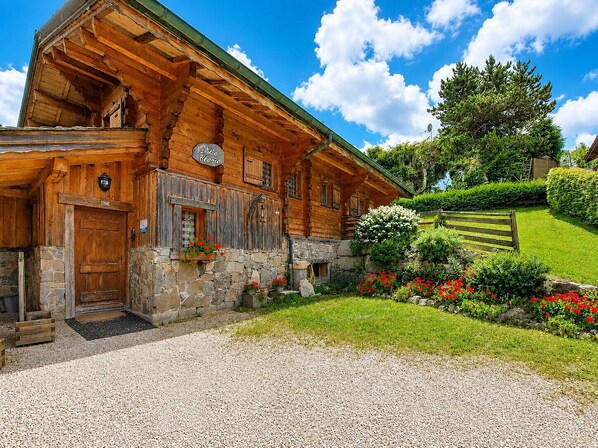 A wooden log cabin with a stone foundation, a wooden door, and a sign that reads 'Le Chalet.'