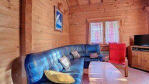 A wooden cabin interior with a blue leather sofa, a wooden table, and a television on a wooden cabinet.