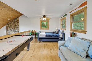 Quarto com mesa de bilhar, sofá, cama e janelas com vista para o verde.