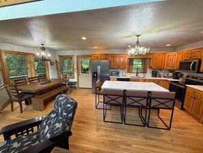 A spacious kitchen with wooden cabinets, a central island, and a dining area with a bench and chairs. - Private Creekside Mountain View Retreat - Hot Tub/Game Room/Fire Pit (Murphy)