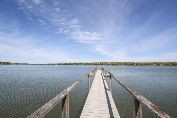 A wooden pier extending into calm water with a clear sky above. - Newly updated spacious steps to water! (Eastham)