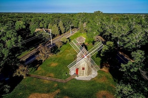 Un moulin à vent entouré d’une zone herbeuse, avec une route et des arbres en arrière-plan.