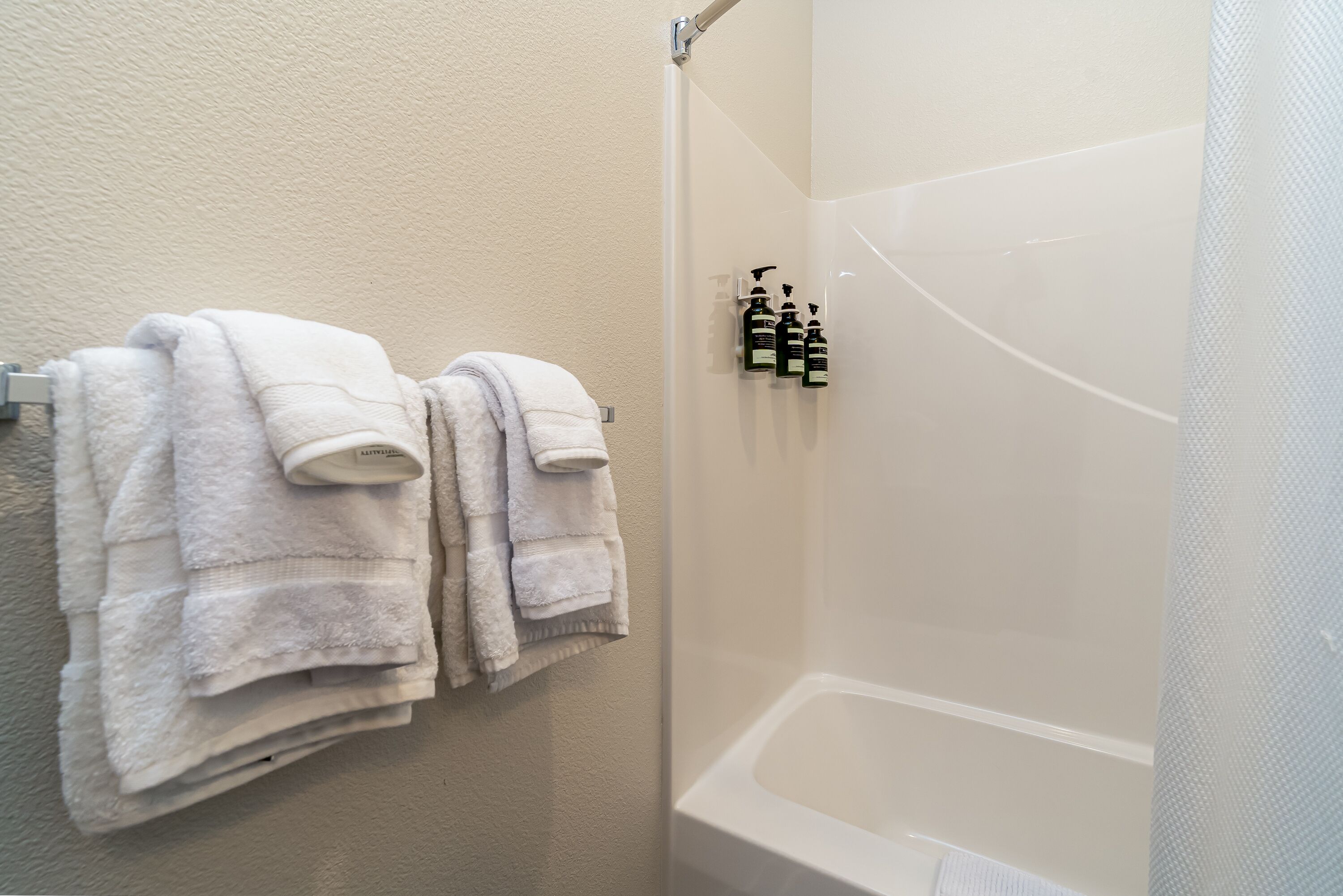 A bathroom with a bathtub, a towel rack with folded towels, and a set of toiletries on the wall.