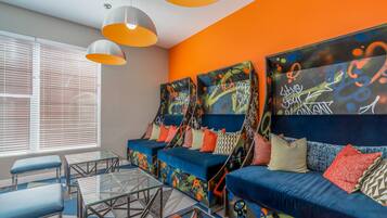 Un espace de détente moderne avec un ensemble de canapés bleus, des tables en verre et des luminaires suspendus orange.
