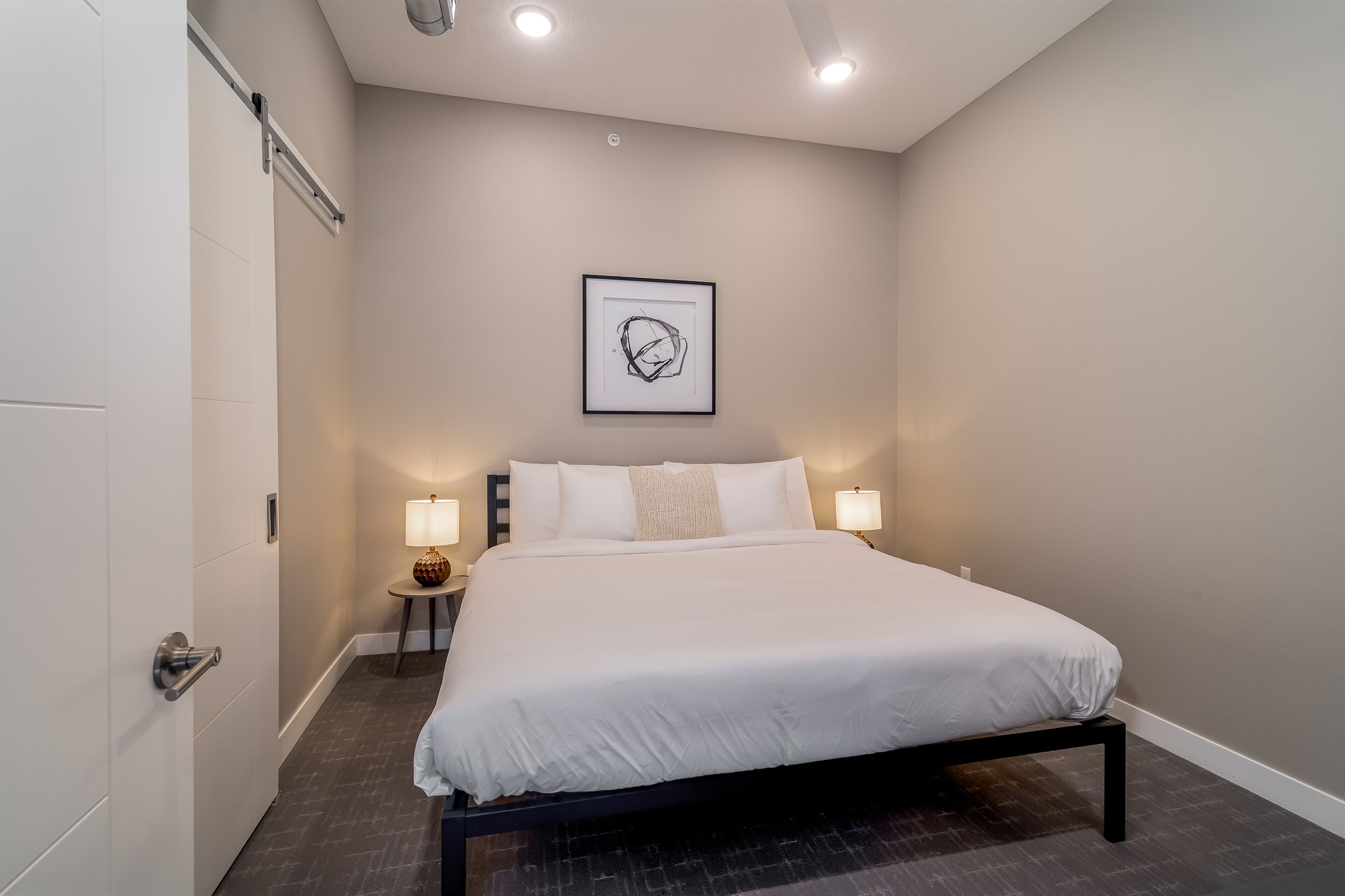 Une chambre d’hôtel moderne avec un grand lit, une œuvre d’art encadrée au mur et deux lampes de chevet.