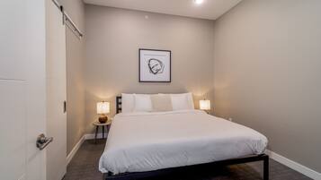Une chambre d’hôtel moderne avec un grand lit, une œuvre d’art encadrée au mur et deux lampes de chevet.