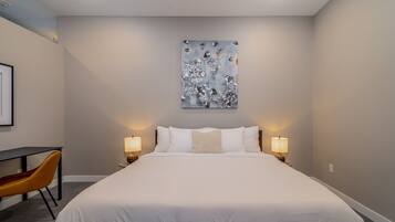 Habitación de hotel con una cama grande, dos lámparas de noche, un escritorio con silla y un cuadro abstracto en la pared.