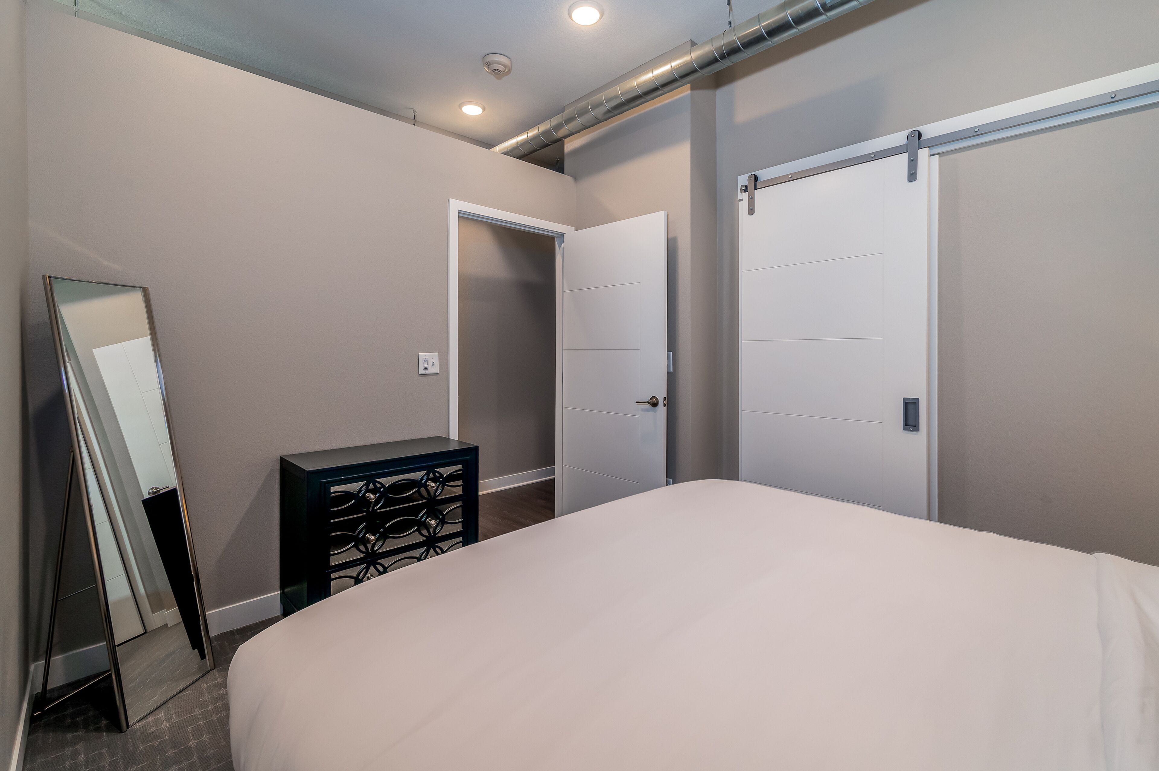 A bedroom with a bed, a dresser, a mirror, and two doors.