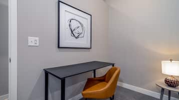 A room with a desk, a framed abstract artwork, a chair, and a lamp.