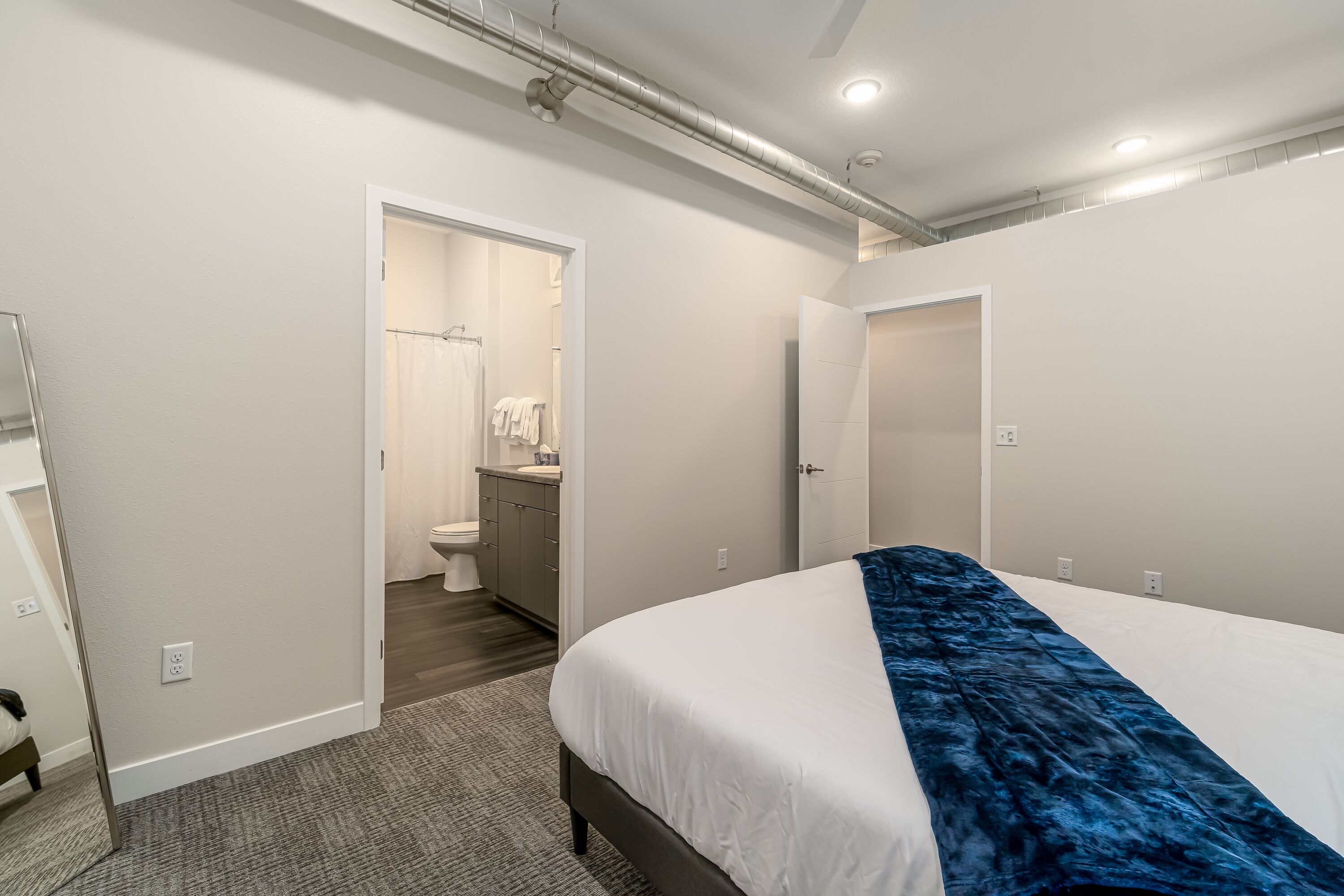 A modern hotel room with a large bed, a bathroom with a shower and toilet, and a walk-in closet.