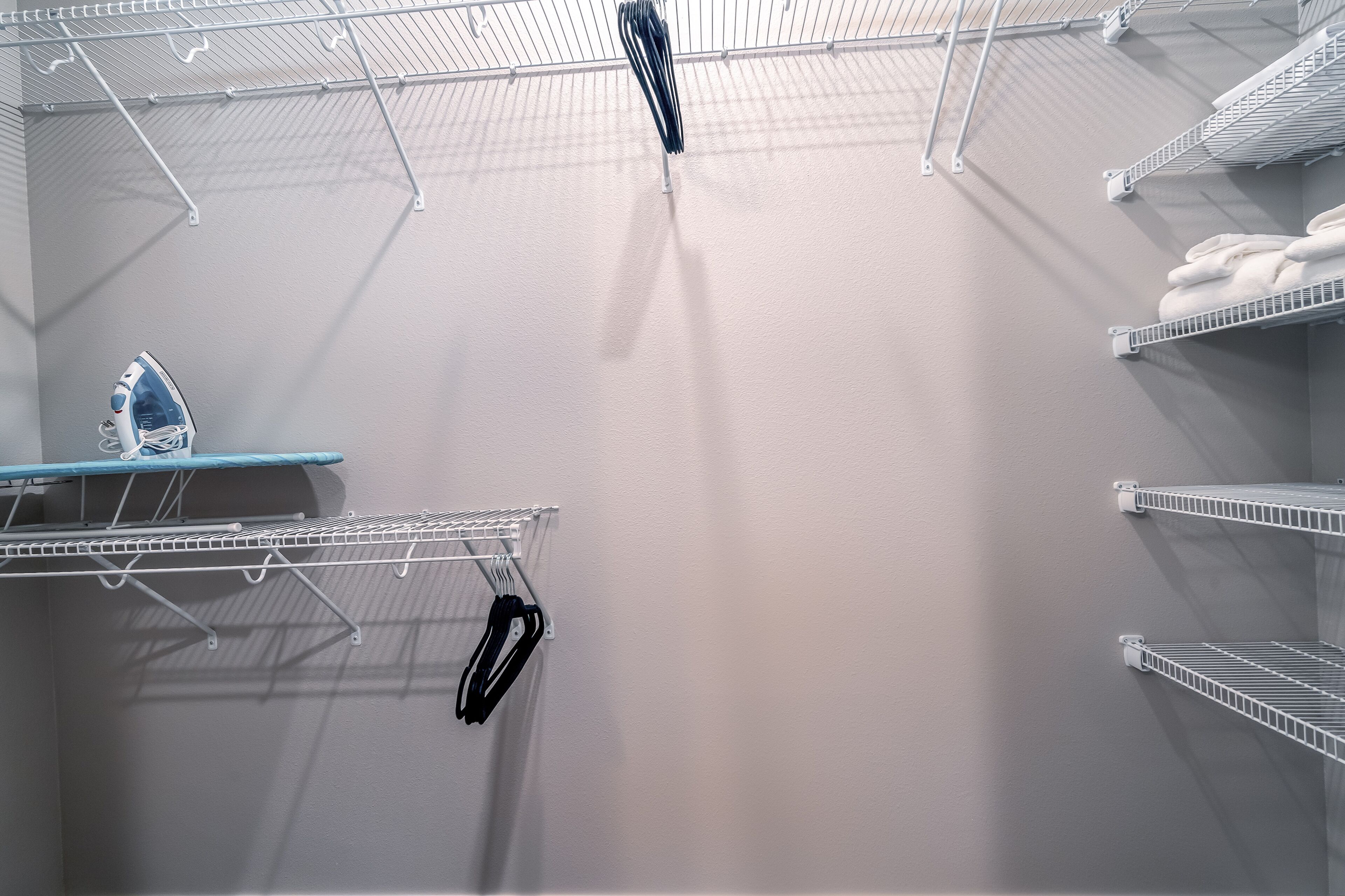 A laundry area with metal shelves, an ironing board, and hanging clothes.