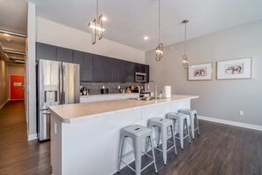 Una cocina moderna con una isla central, taburetes de bar, electrodomésticos de acero inoxidable e iluminación colgante.