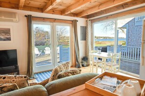 A cozy living room with a television, a sofa, and a dining area with a table and chairs. - Cute Cottage Living by the Sea! (Eastham)