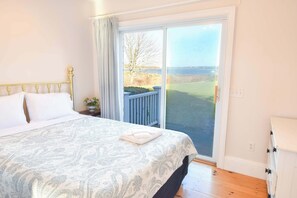 Un dormitorio con cama, mesita de noche, ventana con vistas al exterior y puerta.