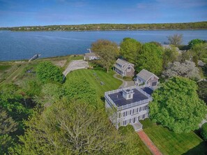 Una casa grande de dos pisos con un amplio jardín y un muelle sobre un lago.