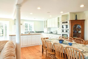 Una cocina amplia con armarios blancos, un comedor con sillas de madera y vistas al exterior.