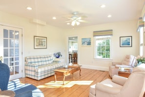 A living room with a plaid sofa, a wooden coffee table, and a ceiling fan. - Quintessential Captain's House w/ Water Views! (Eastham)