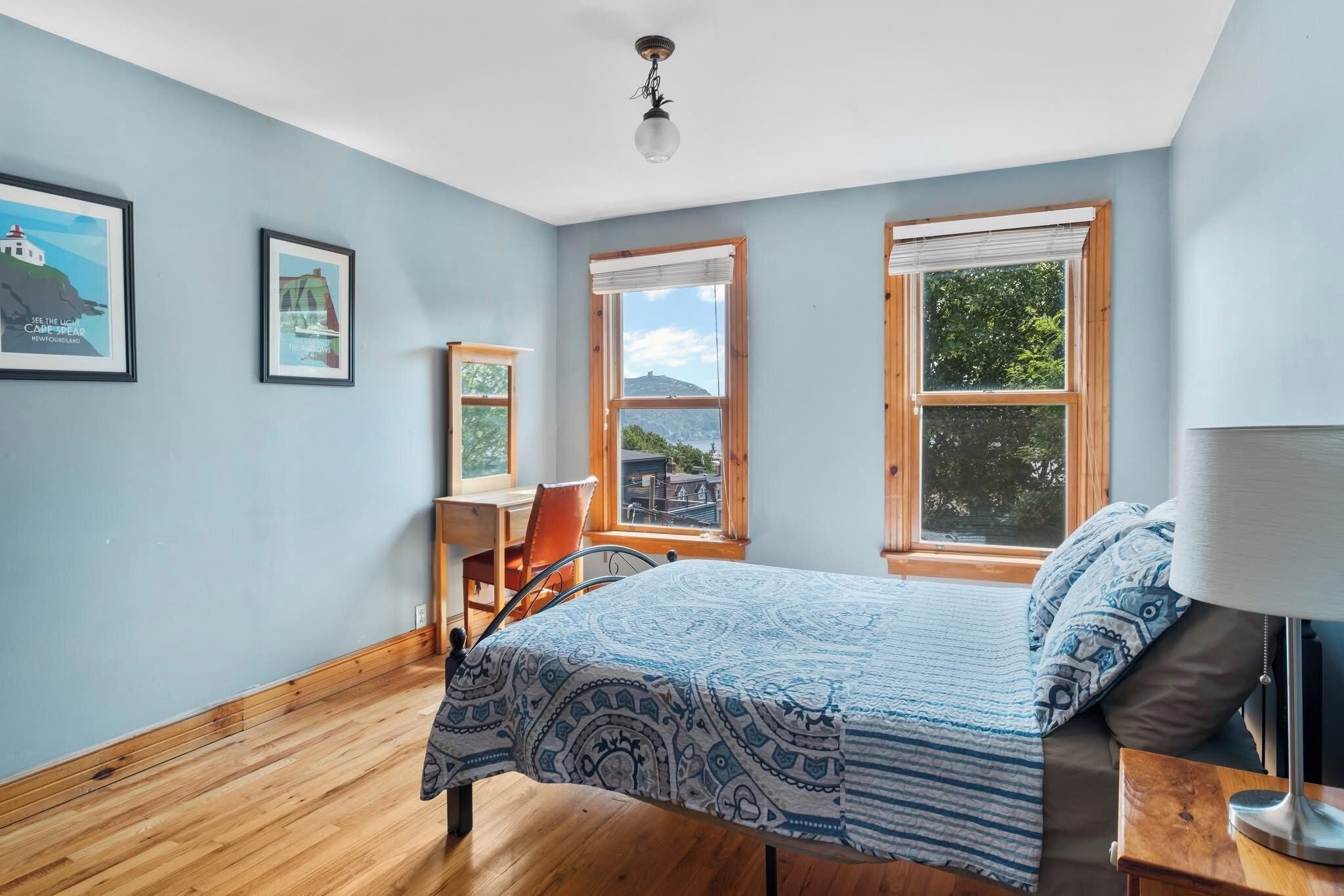 A bedroom with a bed, a desk, and two windows.