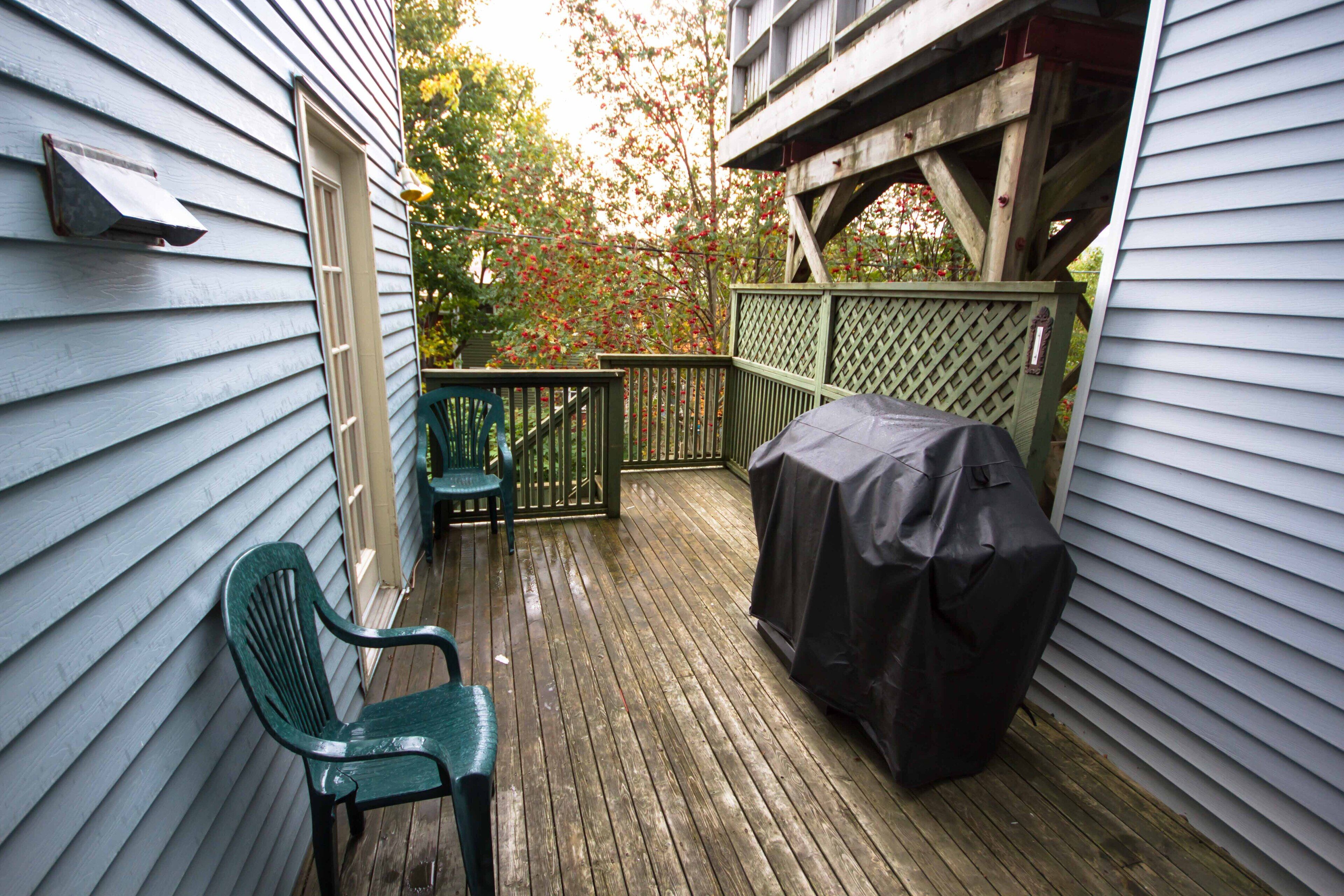 A wooden deck with a covered grill, two green chairs, and a lattice fence.