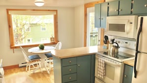 Una cocina compacta con una mesa de comedor, sillas blancas, estufa, microondas y refrigerador.