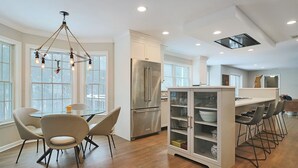Una cocina moderna con comedor, que incluye una araña, un refrigerador y una barra con taburetes.