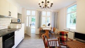 Una cocina con armarios blancos, microondas y estufa. Hay un comedor con mesa y sillas, y un televisor sobre un mueble.