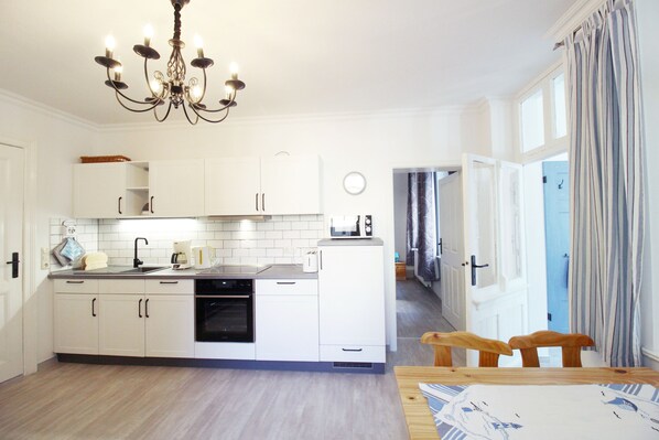 A modern kitchen with white cabinets, a black oven, and a wooden dining table with chairs.