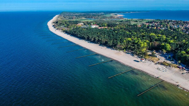 Vista aérea de una zona costera con playa, agua cristalina y abundante vegetación.