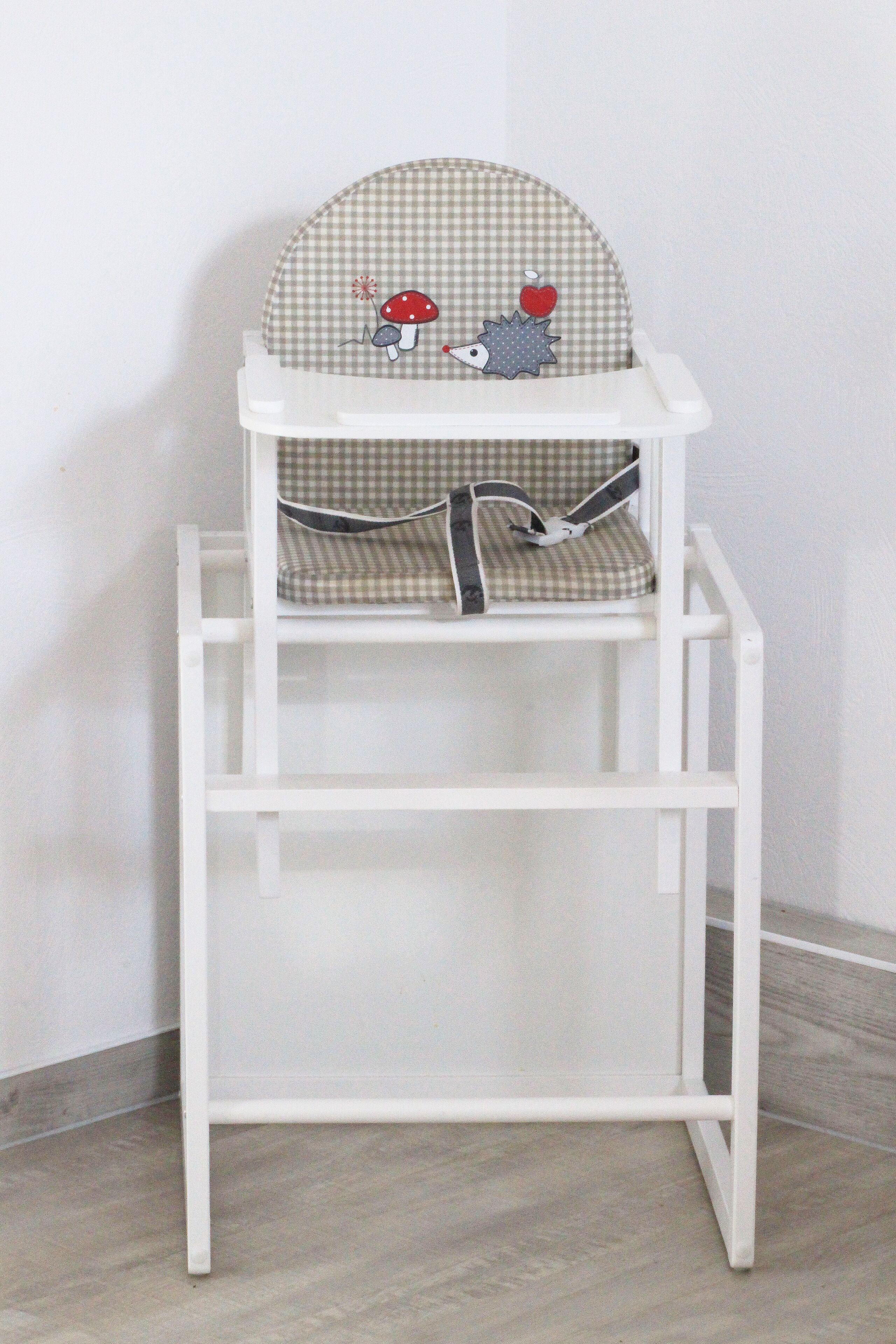 Een witte baby stoel met een geruit zitvlak en een tafelblad.