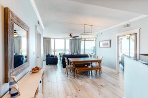 Enjoy meals in the dining area with a wooden table and benches, surrounded by a large mirror and natural light pouring in through large windows.