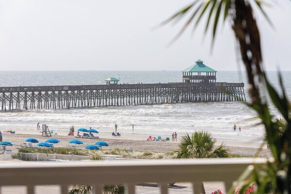 A beach with a pier extending into the ocean, featuring a gazebo and several umbrellas. - San Souci By The Sea | Ocean View 3BR (Folly Beach)