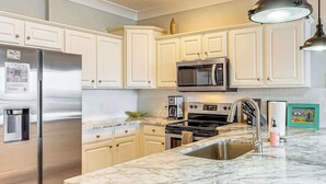 Una cocina moderna con gabinetes blancos, electrodomésticos de acero inoxidable, encimera de mármol y pileta integrada.