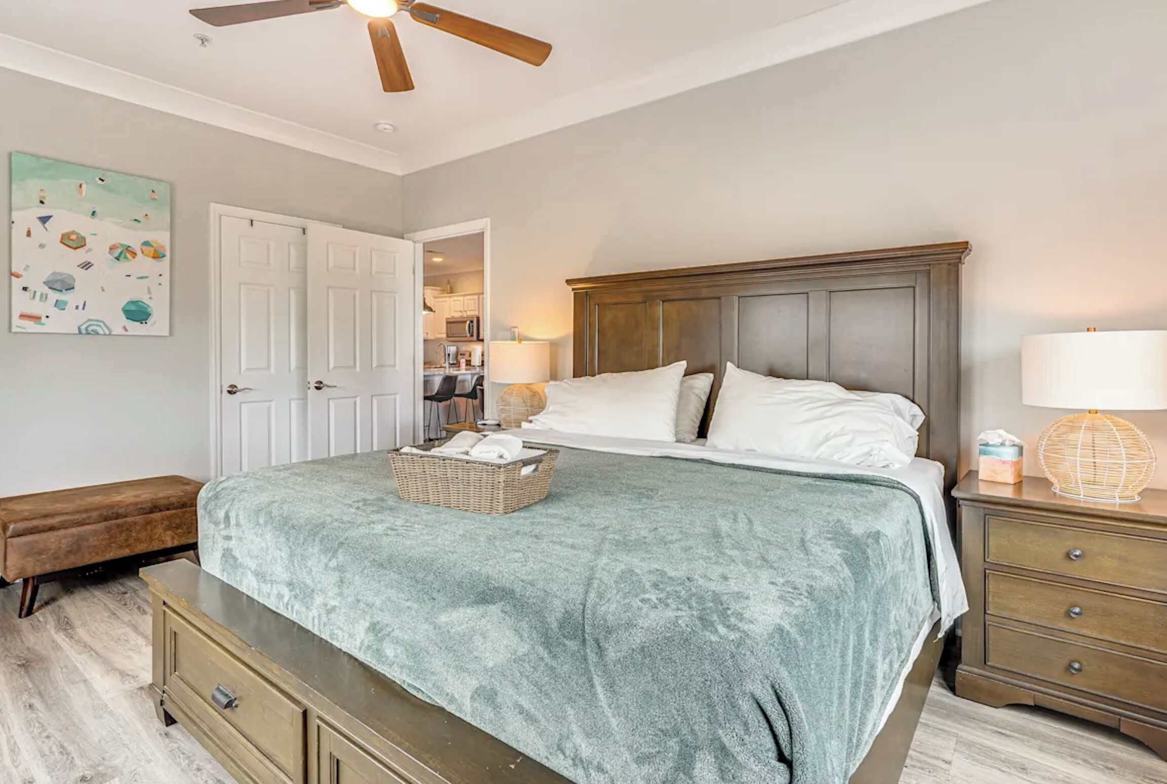Un dormitorio con cama, cabecera de madera, banqueta, mesita de noche, lámpara y ventilador de techo.