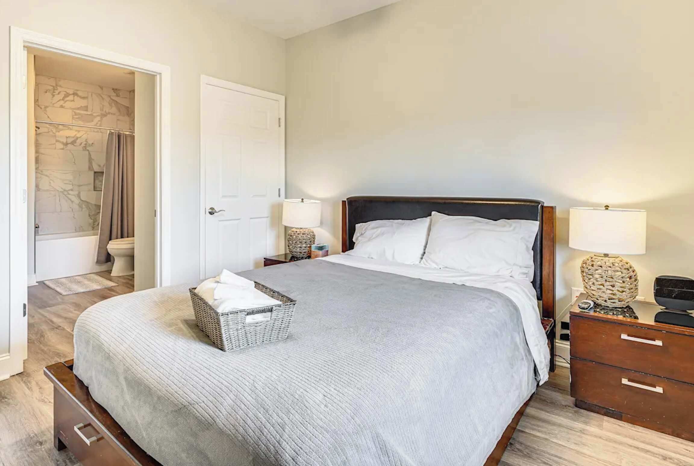 A neatly arranged bedroom with a bed, bedside tables, and a bathroom visible through an open door.