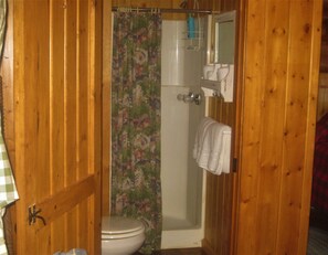 Un baño con paneles de madera, un inodoro, una cortina de ducha y un perchero para toallas.