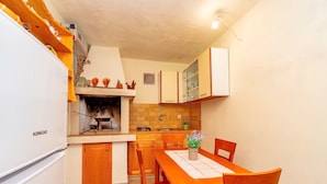 A compact kitchen with a built-in grill, wooden cabinets, and a dining area with a table and chairs.