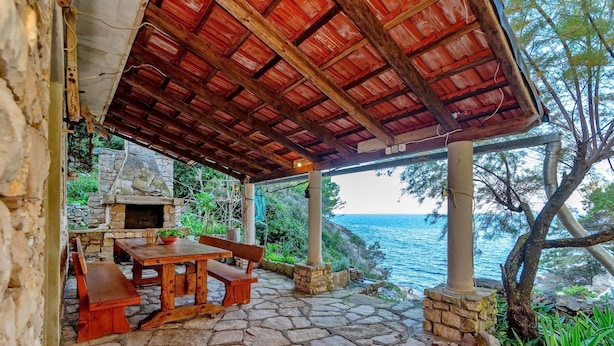 An outdoor patio with stone flooring, wooden furniture, and a stone fireplace.