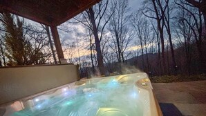 Ett bubbelbad med en glasvägg runt om, omgivet av träd och en solnedgång i bakgrunden.