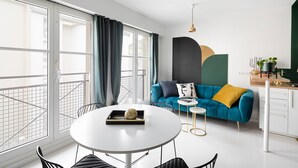 A modern living room with a round white table, a blue sofa with a mustard throw pillow, and a small side table. - Jad'Or - Jolie Duplex avec parking privé (Nantes)