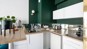 A modern kitchen with white cabinets, a wooden countertop, and a green accent wall. - Jad'Or - Jolie Duplex avec parking privé (Nantes)