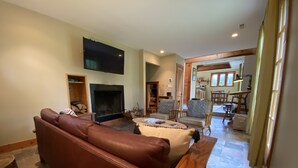 A living room with a brown leather sofa, a wooden coffee table, a flat-screen TV mounted on the wall, and a fireplace. - Charming & cozy in-town retreat in the heart of New Buffalo (New Buffalo)