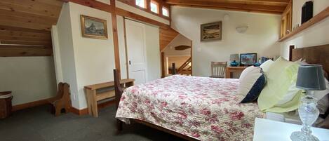 Un dormitorio con techo de madera, una cama con ropa de cama floral, un escritorio y una silla.