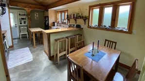 A cozy kitchen with wooden beams, a central island, and a dining area with chairs and a table. - Charming & cozy in-town retreat in the heart of New Buffalo (New Buffalo)