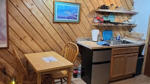 Une cuisine chaleureuse avec des murs en bois, une table à manger, des chaises, un évier et un réfrigérateur.