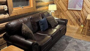 L'intérieur d'un chalet en rondins, avec un canapé en cuir, des tables en bois, un téléviseur fixé au mur et une carte encadrée accrochée au mur.