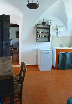 A compact kitchen with a washing machine, a wooden dining table, and a hanging light fixture.